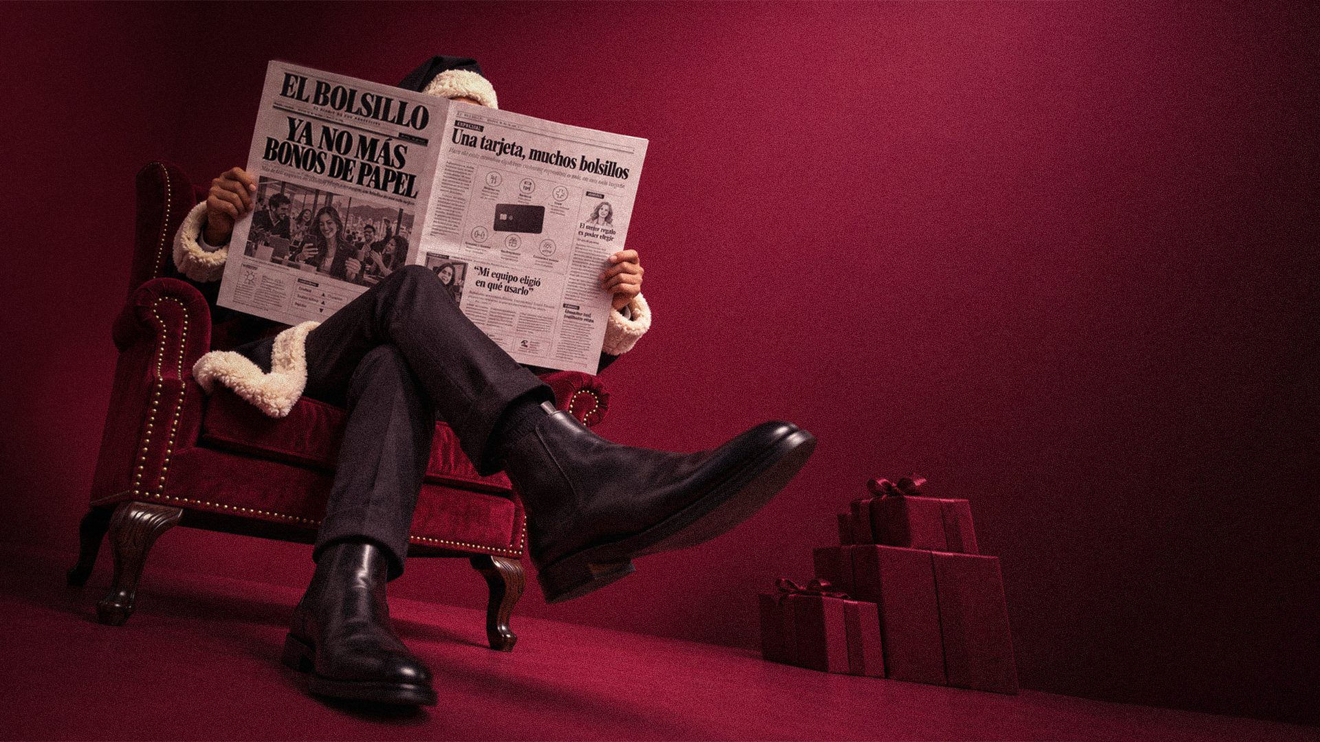 Bin Klaus, el Santa de Bink vestido de negro, lee el periódico El Bolsillo sentado en una poltrona de terciopelo, junto a una pila de regalos.